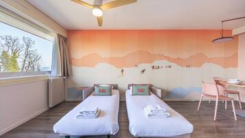 A hotel room with two single beds, a desk, a chair, a ceiling fan, and a large window.