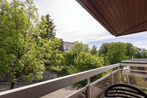 A balcony with a view of trees and a building in the background. - Côté Lac Hostel (Neuvecelle)