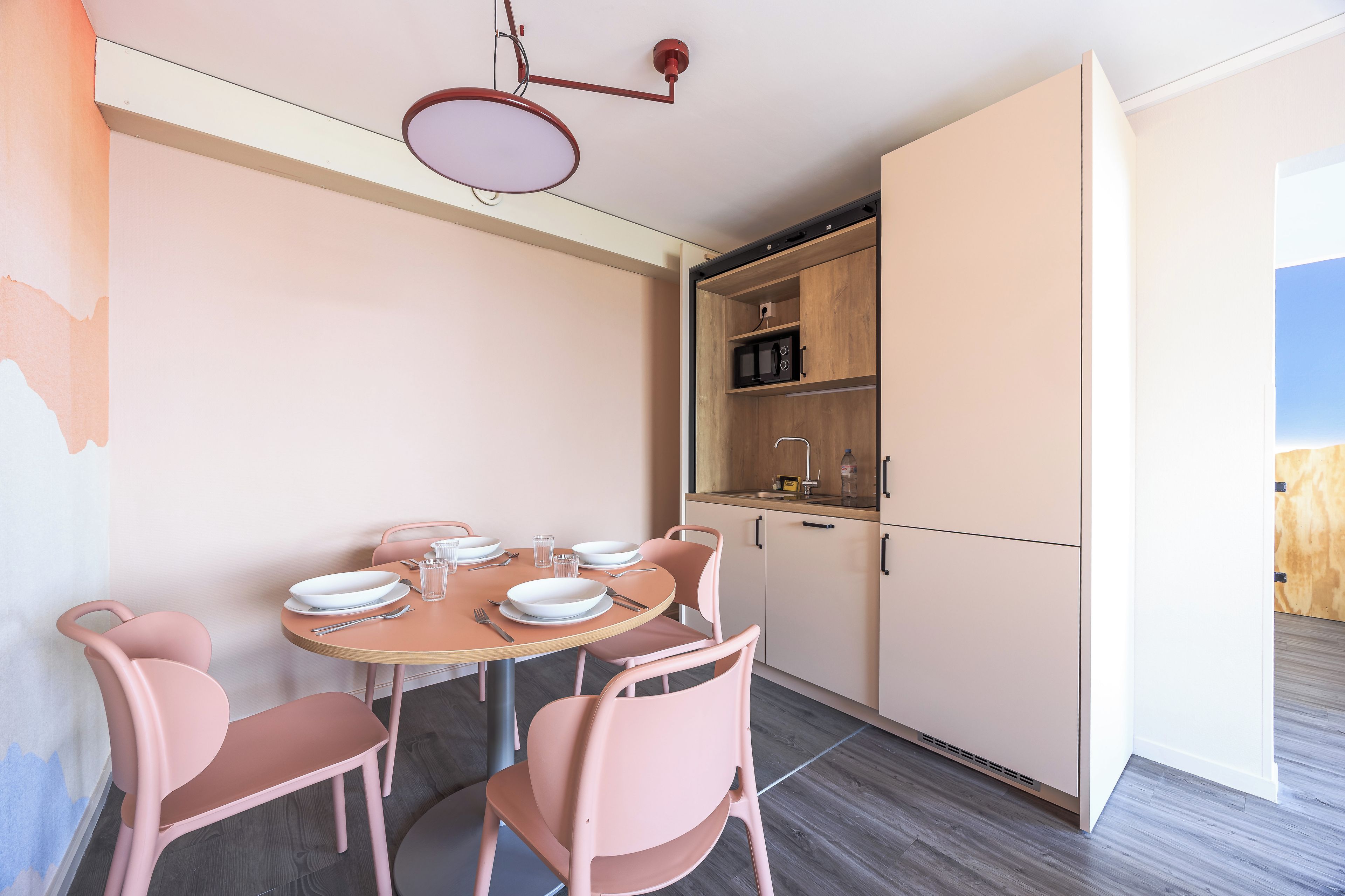 Een eetgedeelte met een ronde tafel, roze stoelen en een witte kast met een magnetron.