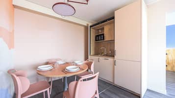 Een eetgedeelte met een ronde tafel, roze stoelen en een witte kast met een magnetron.