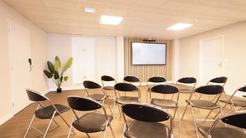 Un salón de conferencias con una pantalla grande, sillas plegables, una planta en maceta y suelo de madera.