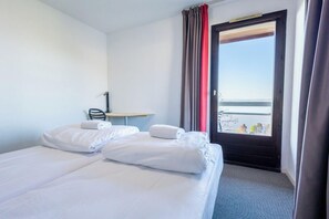 A hotel room with two beds, a desk, and a window with curtains.