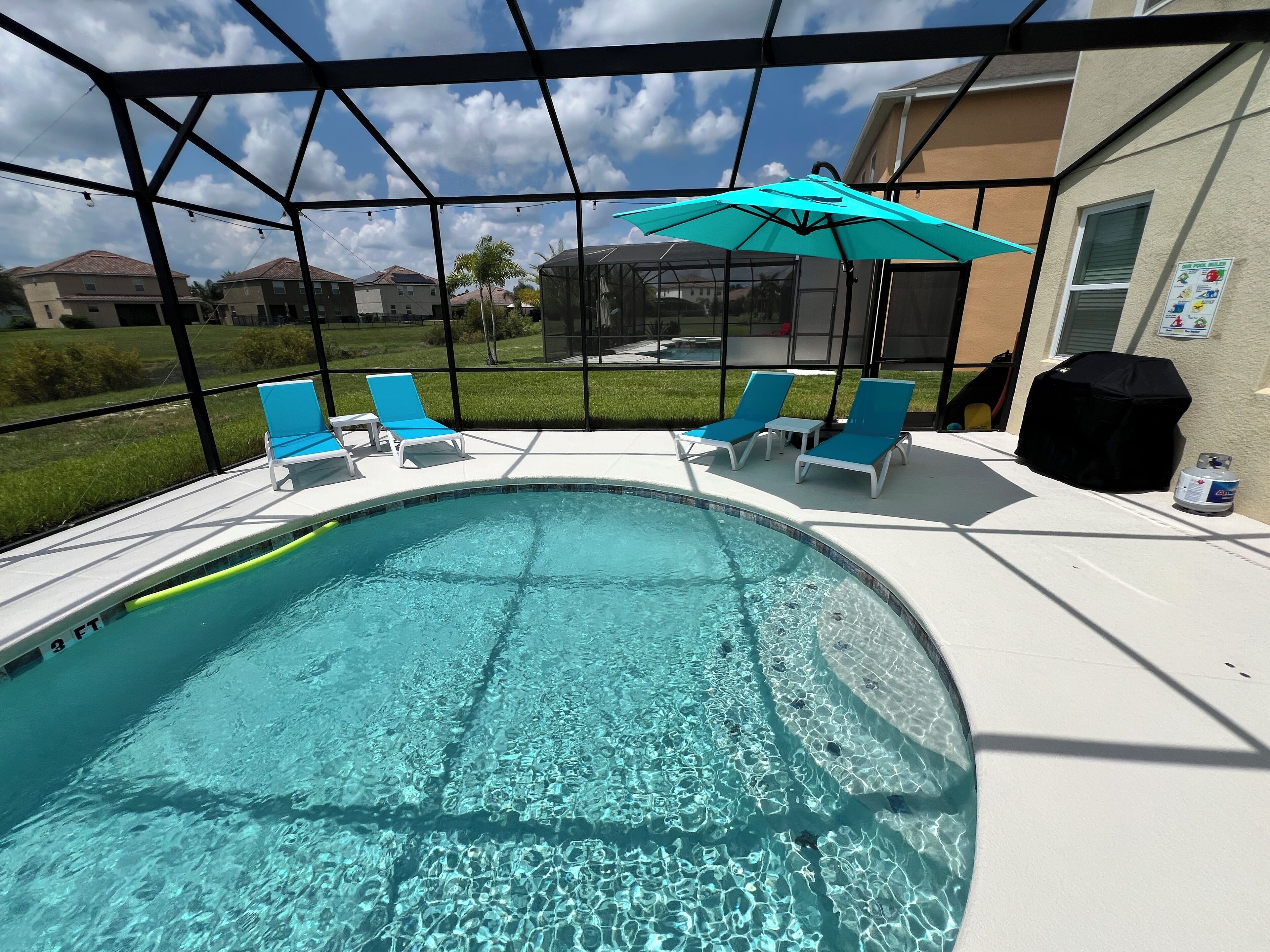 A swimming pool with clear water, surrounded by lounge chairs and a covered grill area.