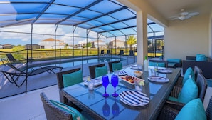 An outdoor patio with a glass enclosure, furnished with tables, chairs, and a pool in the background.