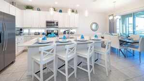A modern kitchen with white cabinetry, a central island with chairs, and a dining area with a view.