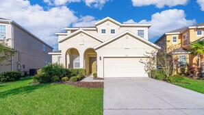 A two-story house with a garage, a front yard with grass, and a clear blue sky.