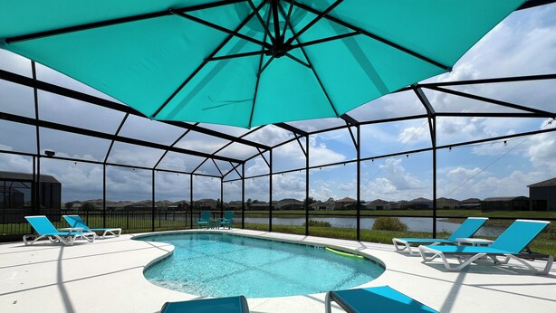 An outdoor pool area with a covered seating area, a pool, and a view of a lake and houses in the background.