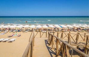 Un paseo marítimo de madera que conduce a una playa con sombrillas blancas y tumbonas.