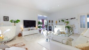 A modern living room with a flat-screen TV, white sofas, a glass coffee table, and decorative plants. - Beautiful home in Rojales (Rojales)