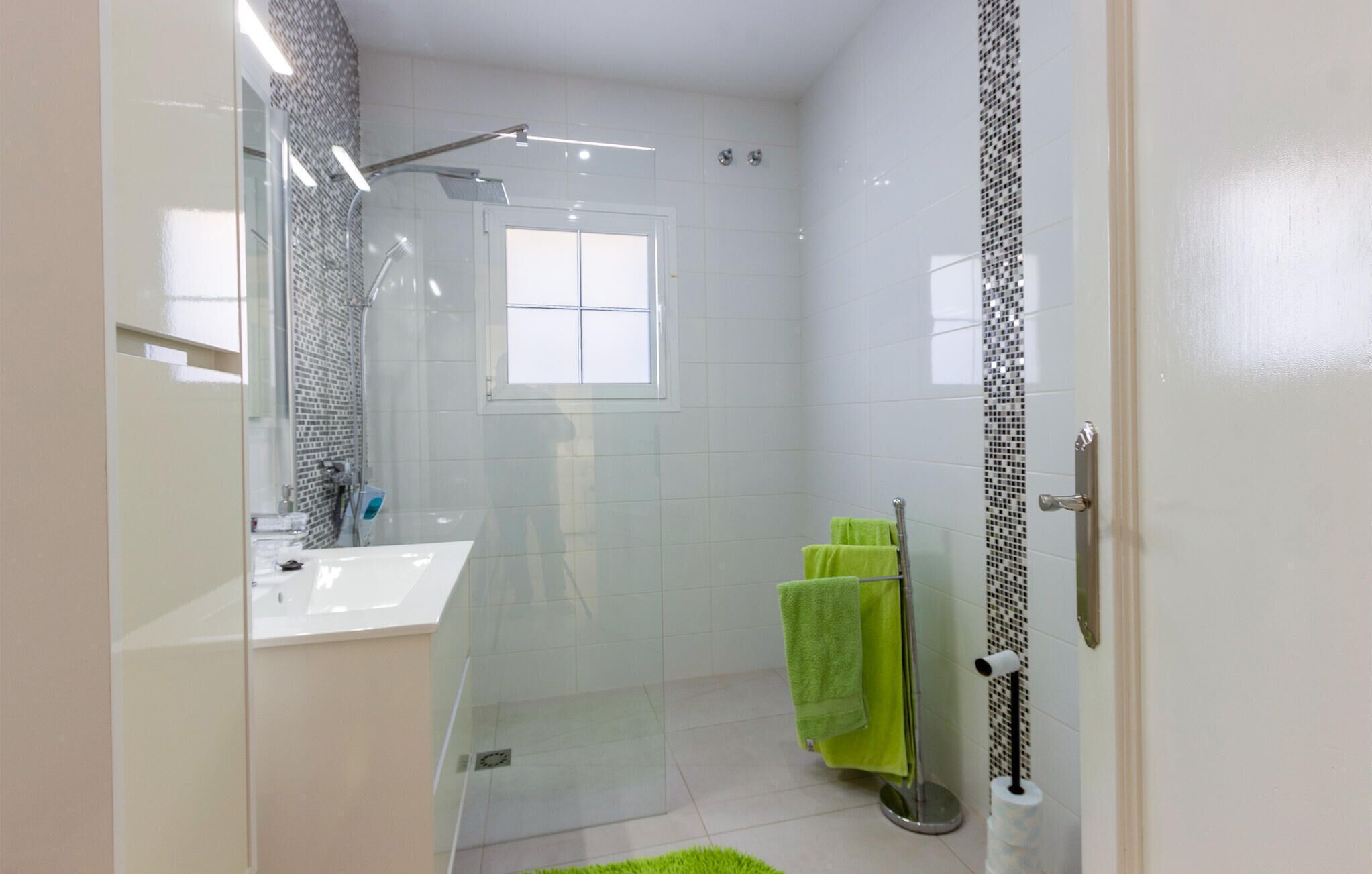 Un bagno moderno con box doccia in vetro, un lavandino bianco e un appendi-asciugamani verde.
