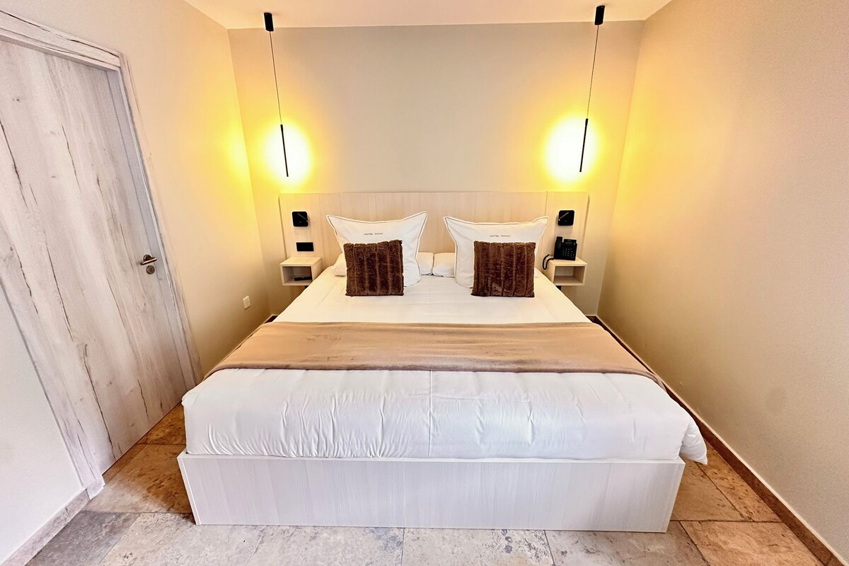 Una habitación de hotel con una cama grande, dos mesitas de noche y una puerta.