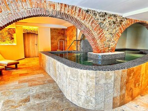 A spa area with a stone wall, a pool, and a wooden bench. - Boutique Hotel Comtal Empuries (Castello d'Empuries)