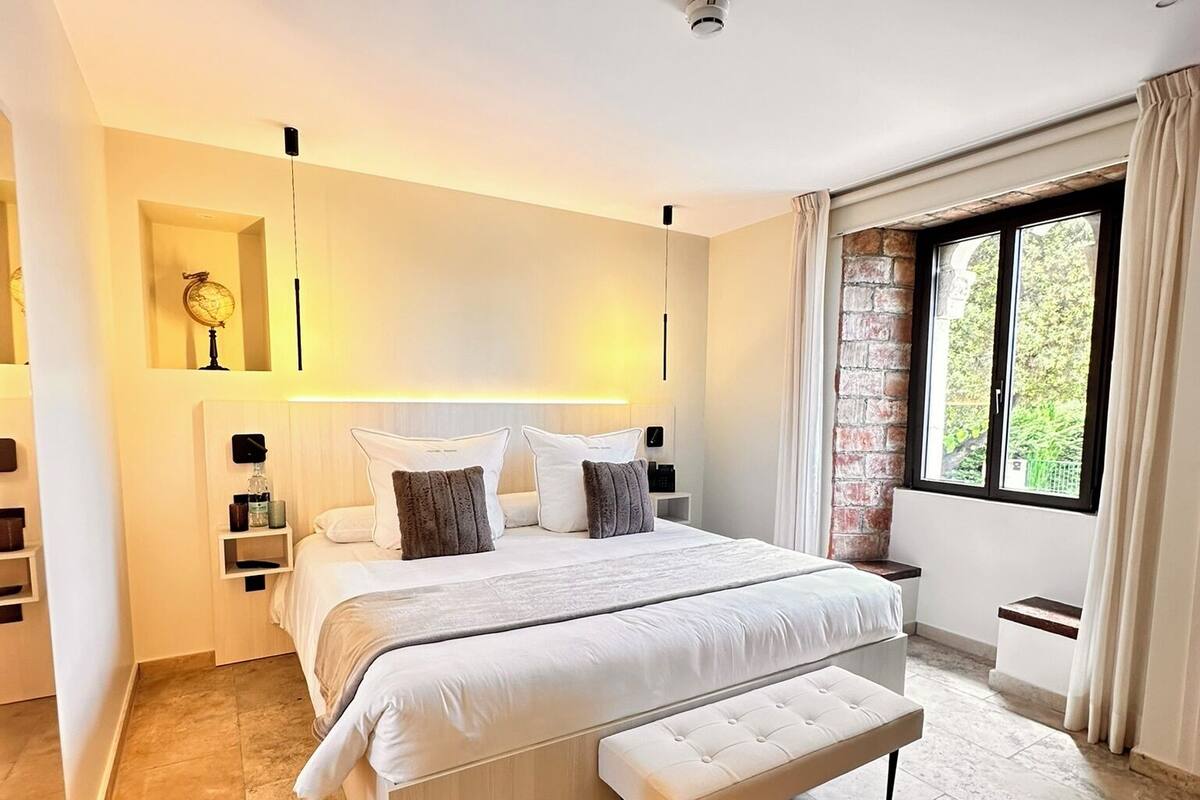 A modern bedroom with a large bed, a bench, a globe on a shelf, and a brick wall.
