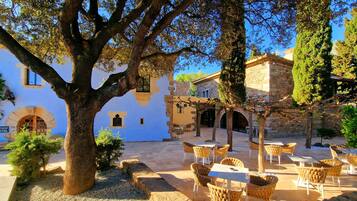 Un patio con mesas al aire libre, edificios de piedra y árboles.