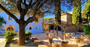 Un patio con mesas al aire libre, edificios de piedra y árboles.