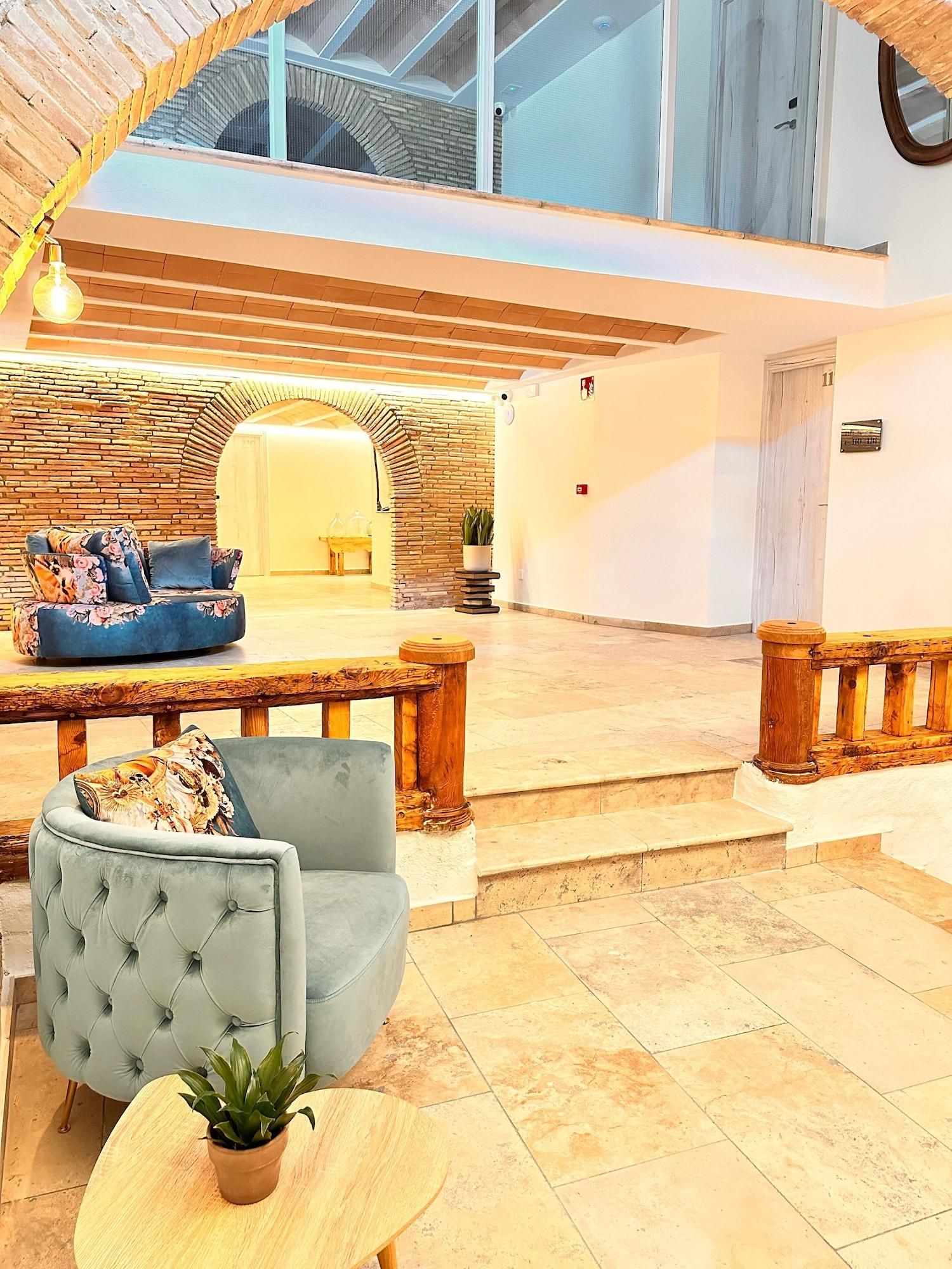A spacious, modern interior with a high ceiling, a seating area with a sofa and armchairs, and a staircase leading to an upper level.