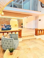 Un interior espacioso y moderno con un techo alto, una zona de estar con sofá y sillones, y una escalera que conduce a un nivel superior.