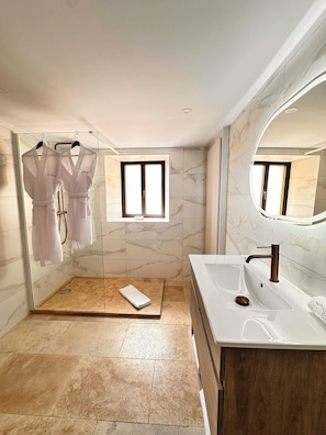 Un bany modern amb una cabina de dutxa de vidre, un lavabo amb un gran mirall i una finestra petita.