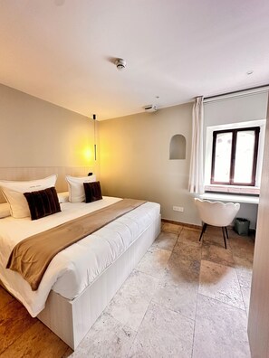 Habitació d'hotel amb un llit gran, una taula de nit, una cadira, una finestra i un aire condicionat fixat a la paret.