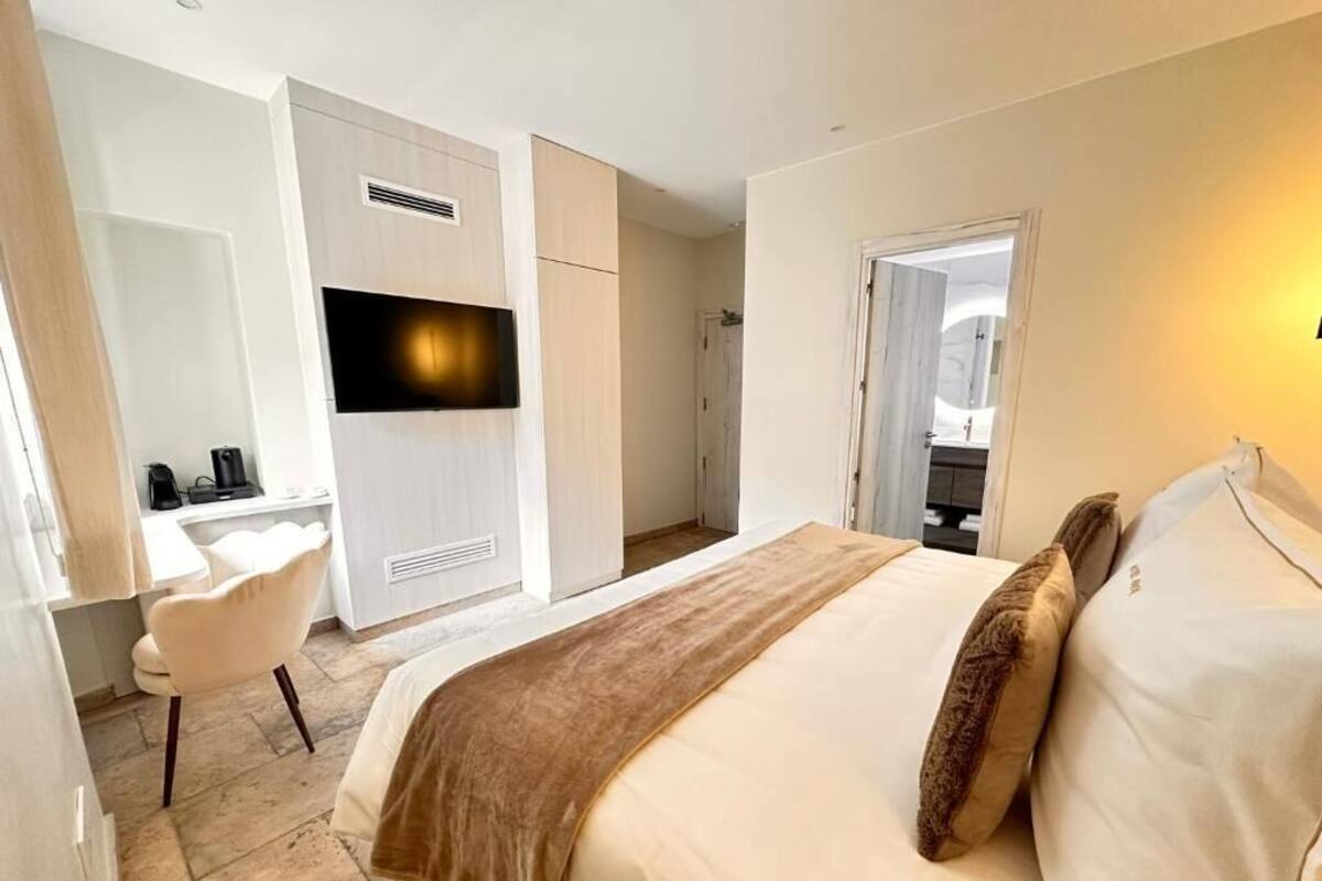 A hotel room with a bed, a desk, a chair, a TV, and a bathroom visible through an open door.