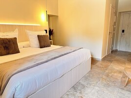 Habitación de hotel con una cama grande, una mesita de noche y una puerta que da a otra habitación.