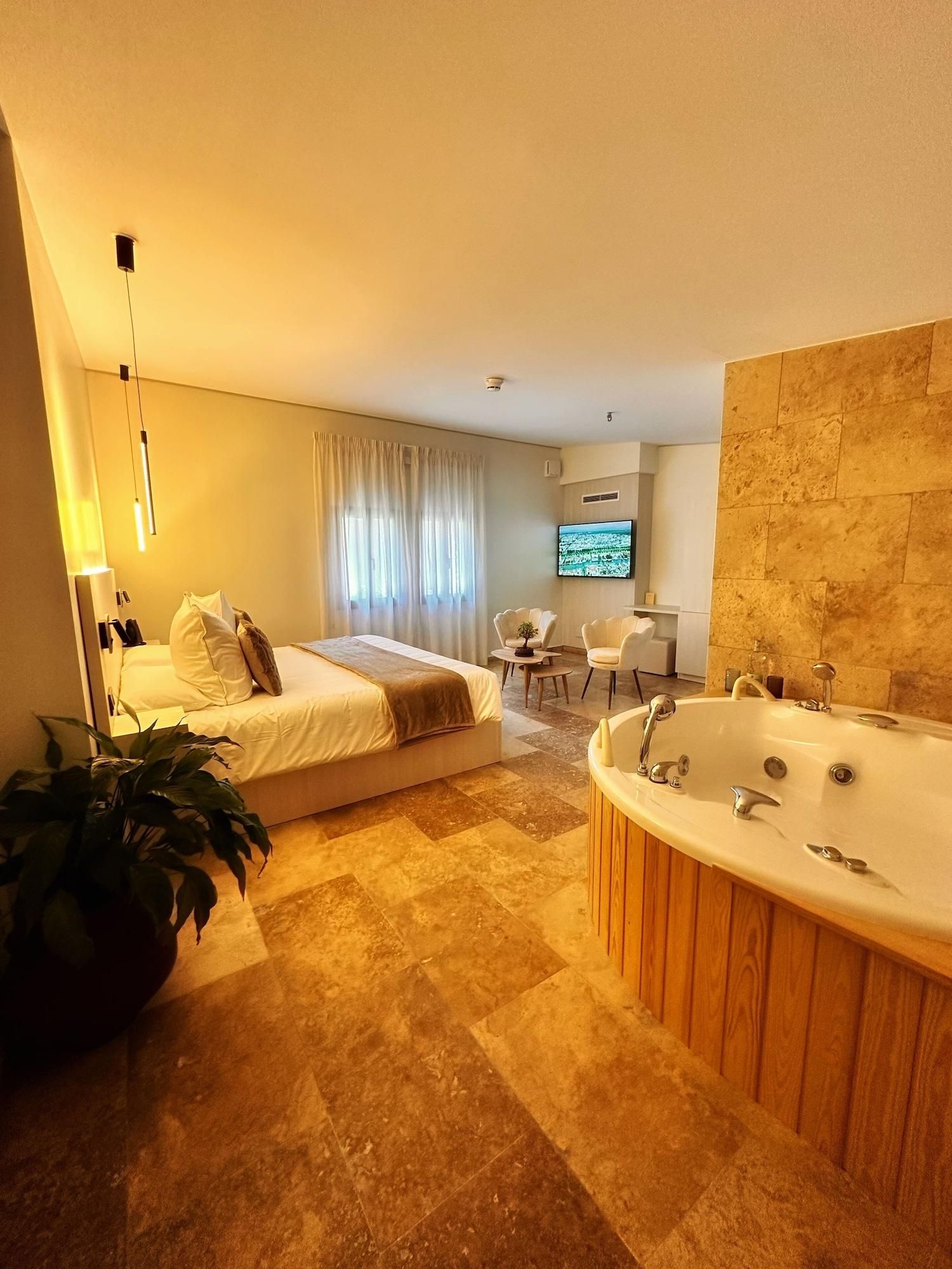 Habitación de hotel moderna con una cama grande, una zona de estar con televisor y un baño separado con bañera.