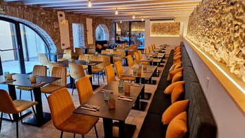 Un restaurante con mesas largas y cabinas, paredes de piedra y vistas amplias a través de grandes ventanales.