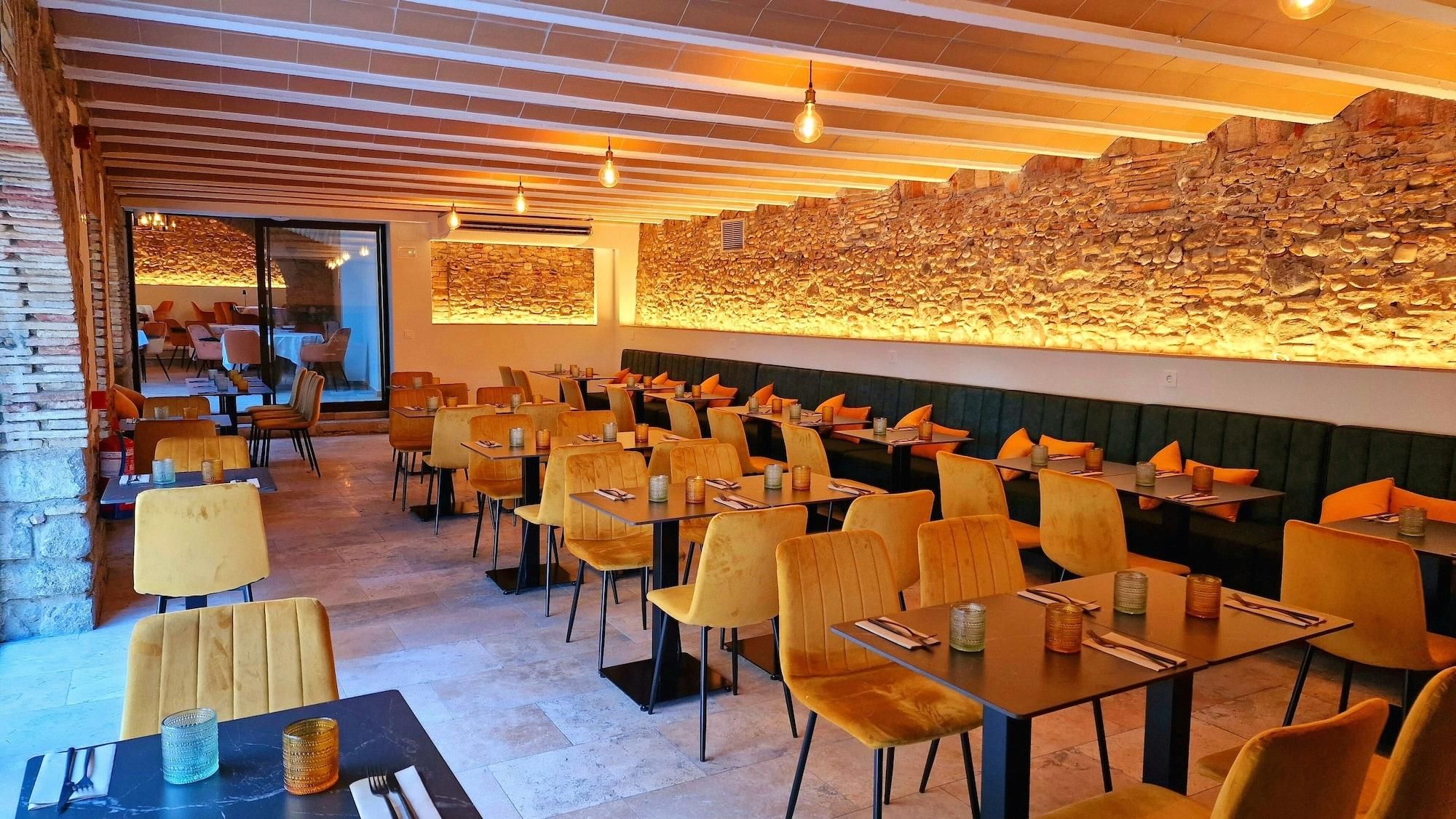 Restaurante com parede de pedra, cadeiras amarelas e mesas.