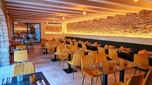 Un restaurante con pared de piedra, sillas amarillas y mesas.