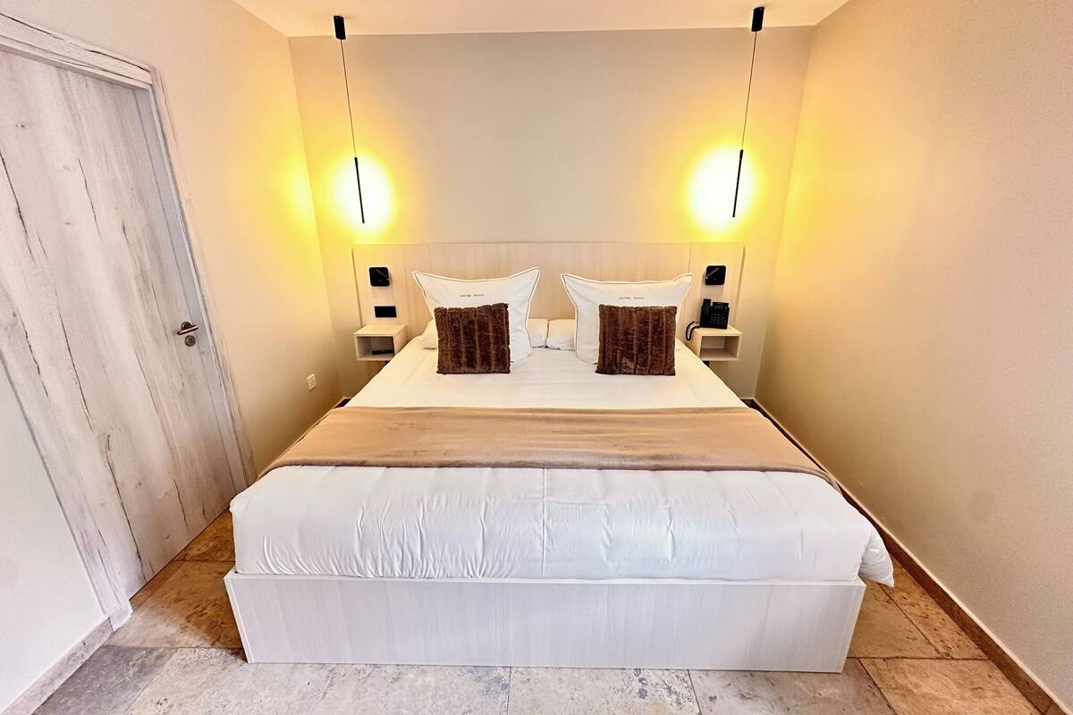 A hotel room with a large bed, two bedside tables, a nightstand, and a door.