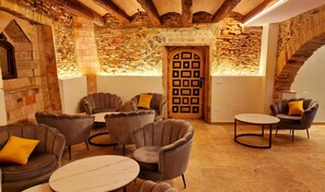 A cozy interior with stone walls, a wooden door with geometric patterns, and comfortable seating. - Boutique Hotel Comtal Empuries (Castello d'Empuries)