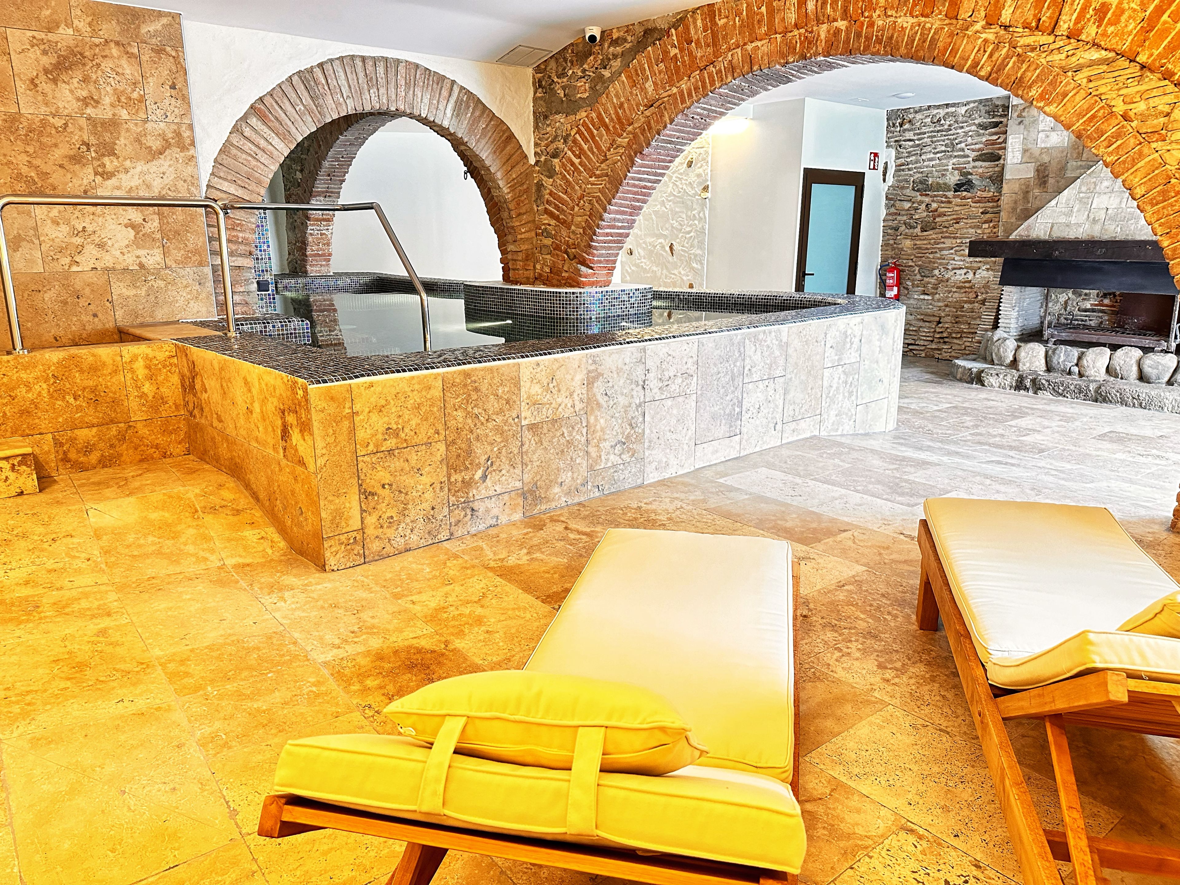 Un área de spa con una bañera de hidromasaje, dos sillones amarillos y una chimenea de piedra.
