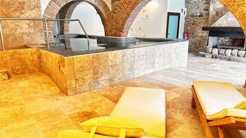 Un área de spa con una bañera de hidromasaje, dos sillones amarillos y una chimenea de piedra.