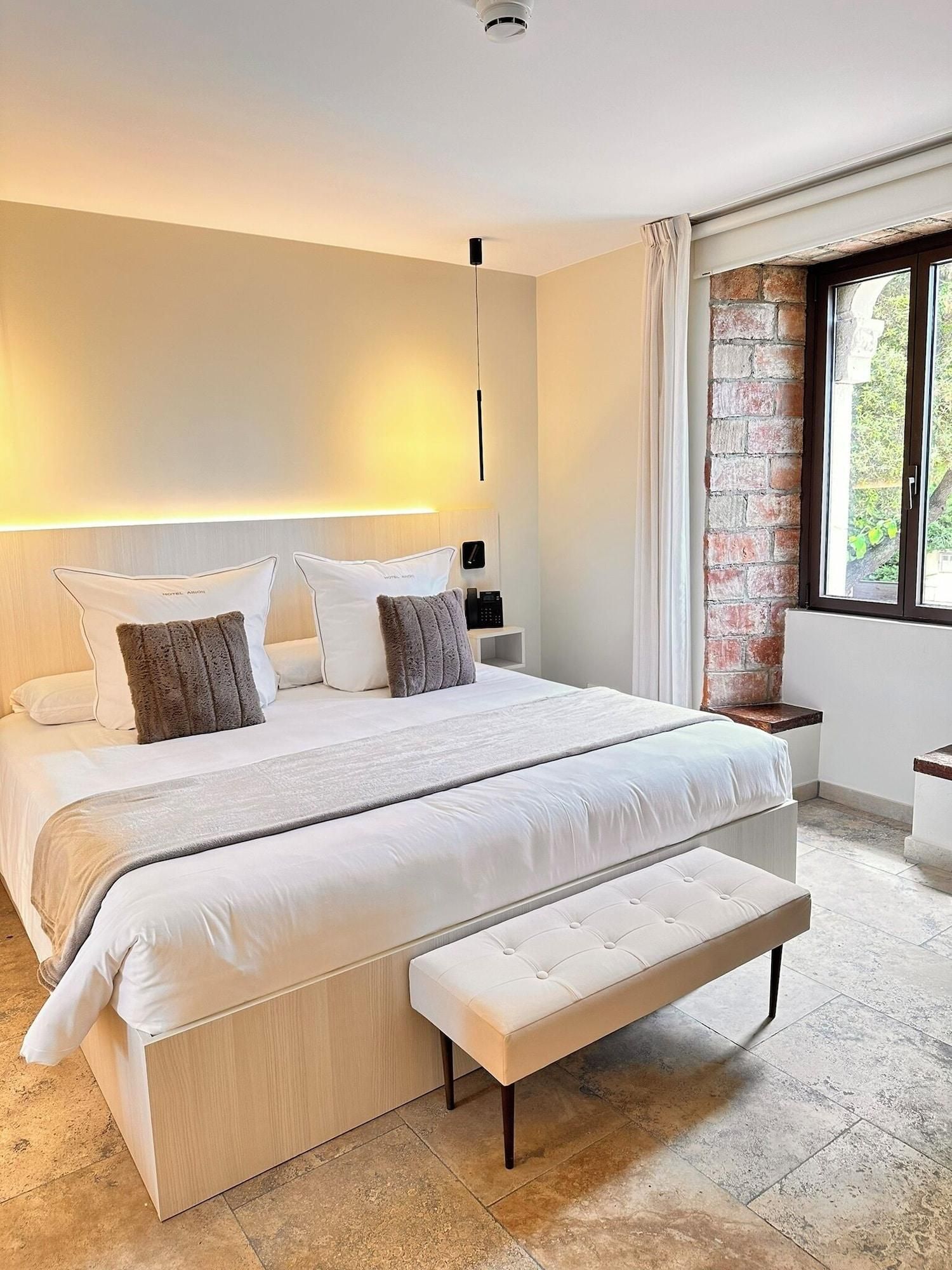 Un dormitorio moderno con una cama grande, mesitas de noche, un banco y una pared de ladrillo.