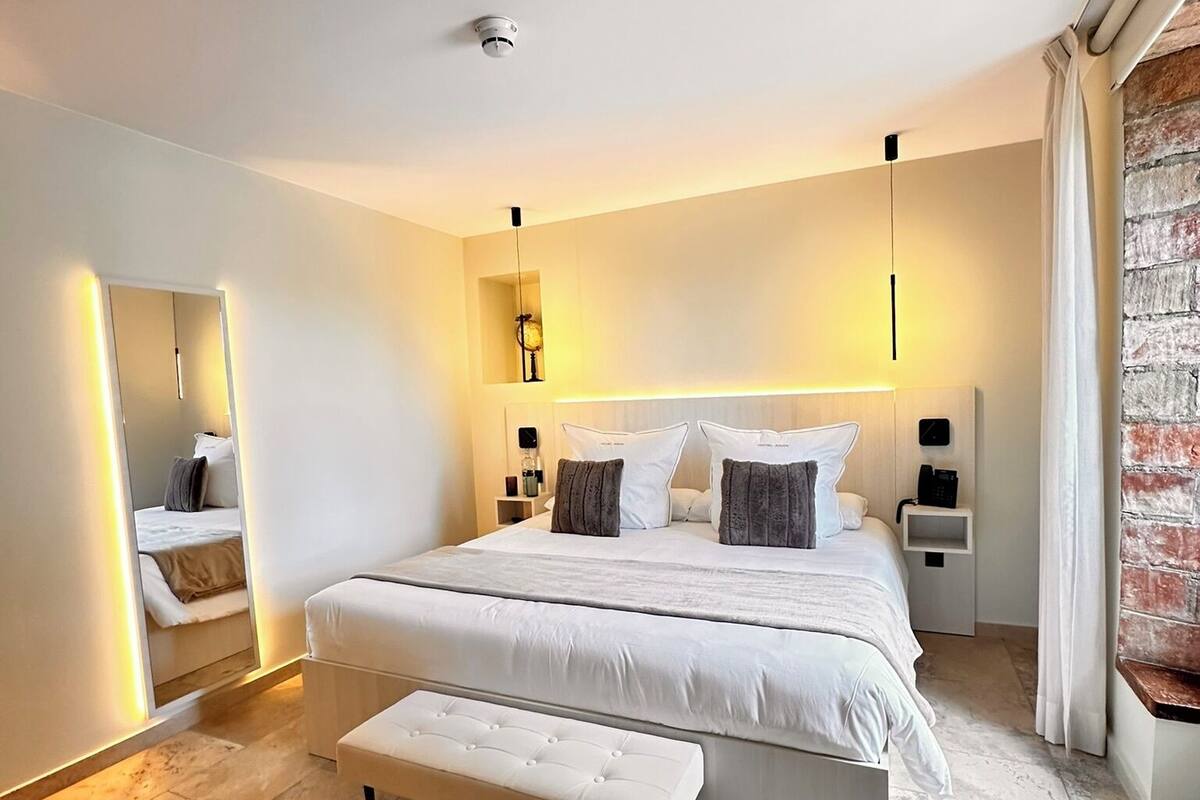 A modern bedroom with a large bed, bedside tables, a bench, and a mirror.