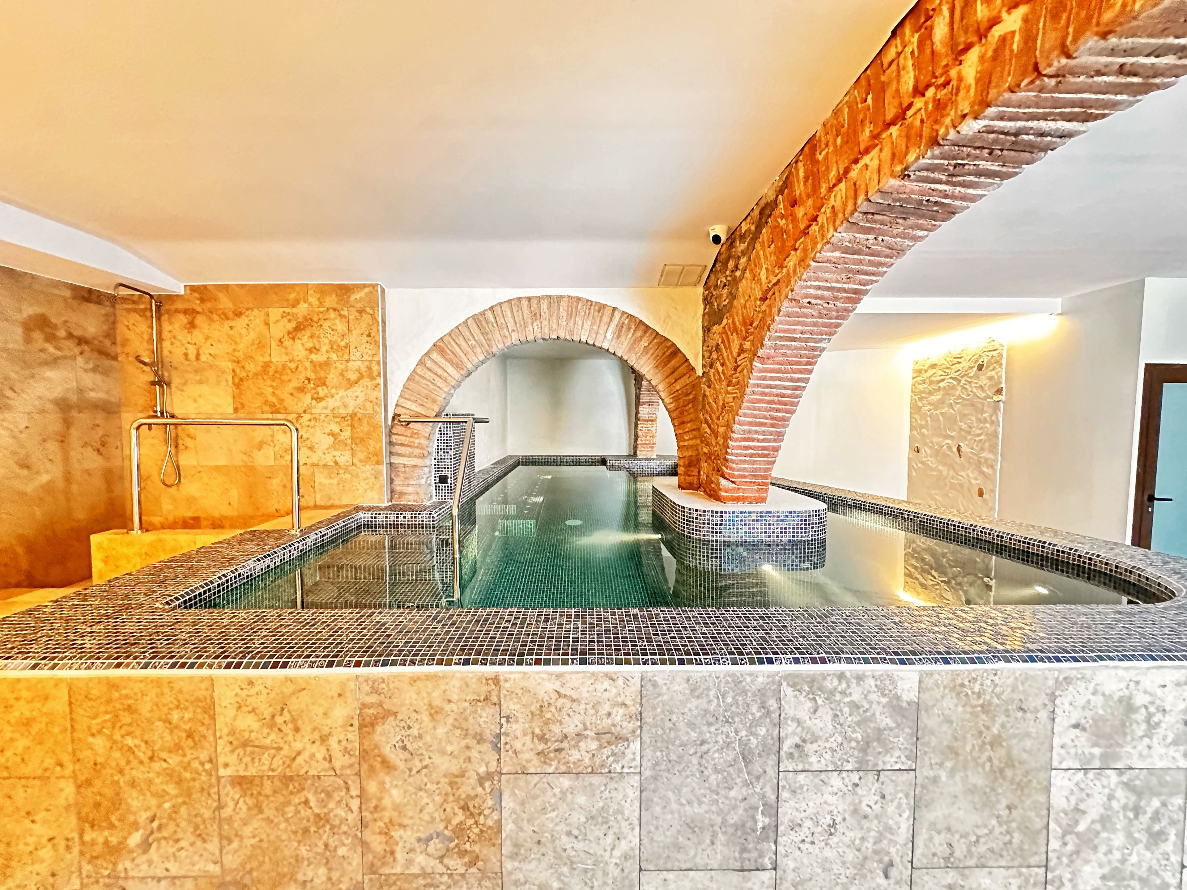 A spa area with a glass-enclosed hot tub, stone walls, and a wooden archway.
