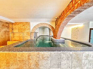 Un área de spa con un jacuzzi de paredes de cristal, paredes de piedra y un arco de madera.