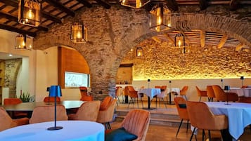 Un restaurant doté d’arches en pierre, de tables recouvertes de nappes blanches et de chaises orange.
