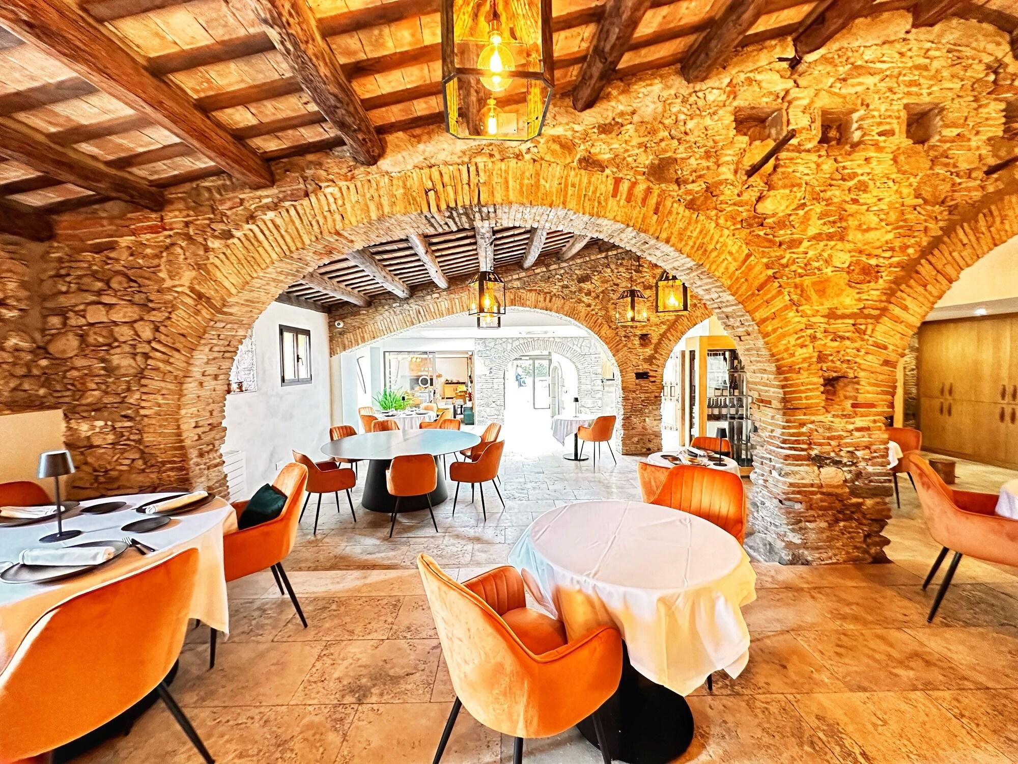 Een restaurant met stenen bogen en houten balken, met ronde tafels en oranje stoelen.