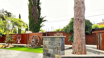 Un patio con una jardinera de piedra, un árbol grande y una valla metálica decorativa.