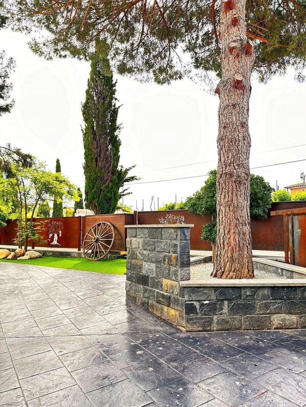 Un patio con una jardinera de piedra, un árbol grande y una valla metálica decorativa.