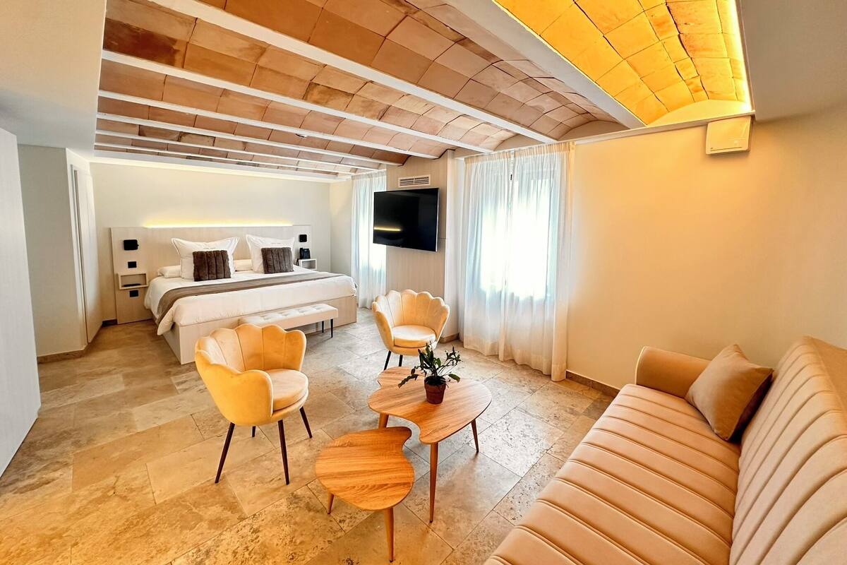 A modern hotel room with a bed, two armchairs, a sofa, a small wooden table, and a TV.