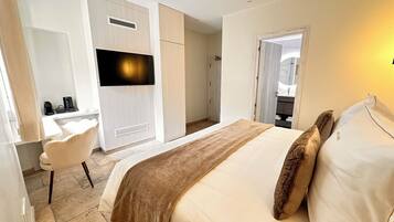 Habitación de hotel con cama, escritorio, silla, televisor y baño visible a través de una puerta abierta.