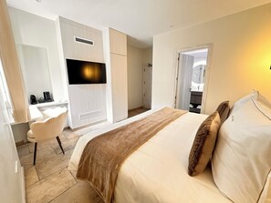 Habitación de hotel con cama, escritorio, silla, televisor y baño visible a través de una puerta abierta.