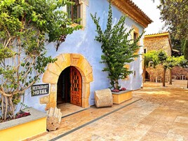 Un edificio con un arco de piedra en la entrada, un letrero que indica restaurante y hotel boutique, y un área de estar al aire libre con mesas y sillas de piedra.