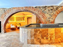 Un área de spa con un arco de piedra, una bañera de hidromasaje y una sala de masajes.