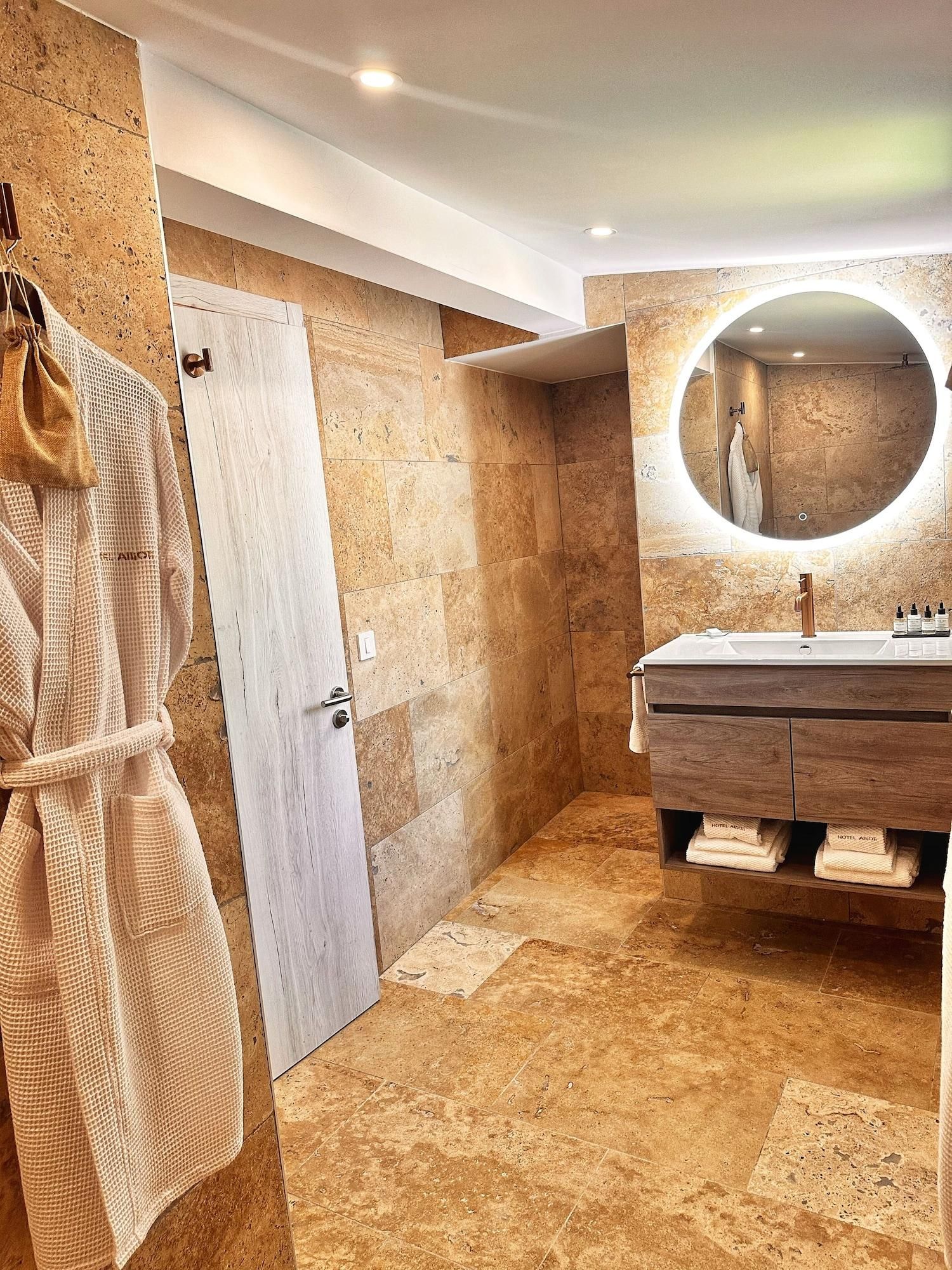 A modern bathroom with a wooden vanity, a round mirror, and a robe hanging on the wall.