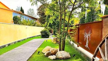 Un jardín bien cuidado con un camino empedrado, un árbol y una valla metálica decorativa.