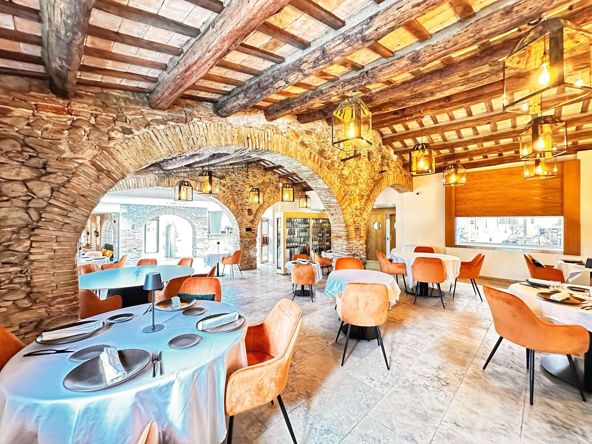 Un restaurante con arcos de piedra, vigas de madera y mesas con sillas anaranjadas.