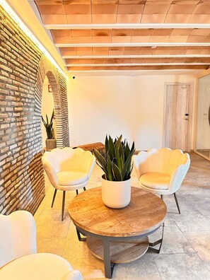Un interior moderno con pared de ladrillo, dos sillas blancas, una mesa redonda de madera y una planta en maceta.